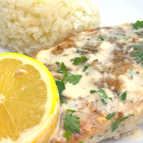 Creamy lemon chicken on a plate with a rounded scoop of rice and a lemon round.