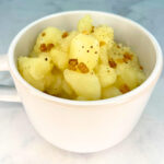 COMPLETED STEWED POTATOES TOPPED WITH BACON IN A WHITE CUP.
