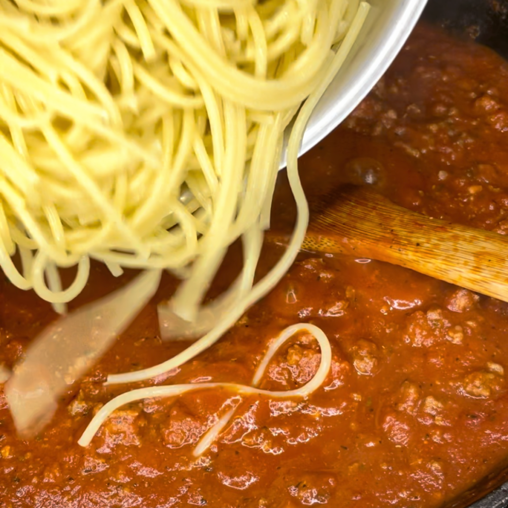 dumping the cooked noodles into the sauce mixture in the cast iron pan
