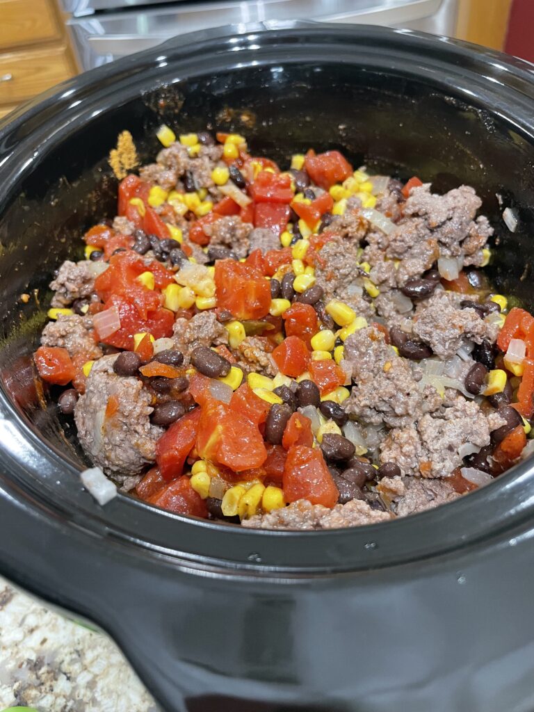 Crock pot full of ground beef, black beans, corn, tomatoes, and chilies.
