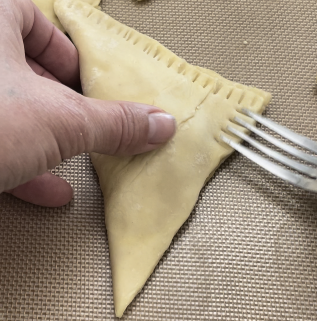 Crimping the edges of the pastry with a fork after closing it into a triangle.