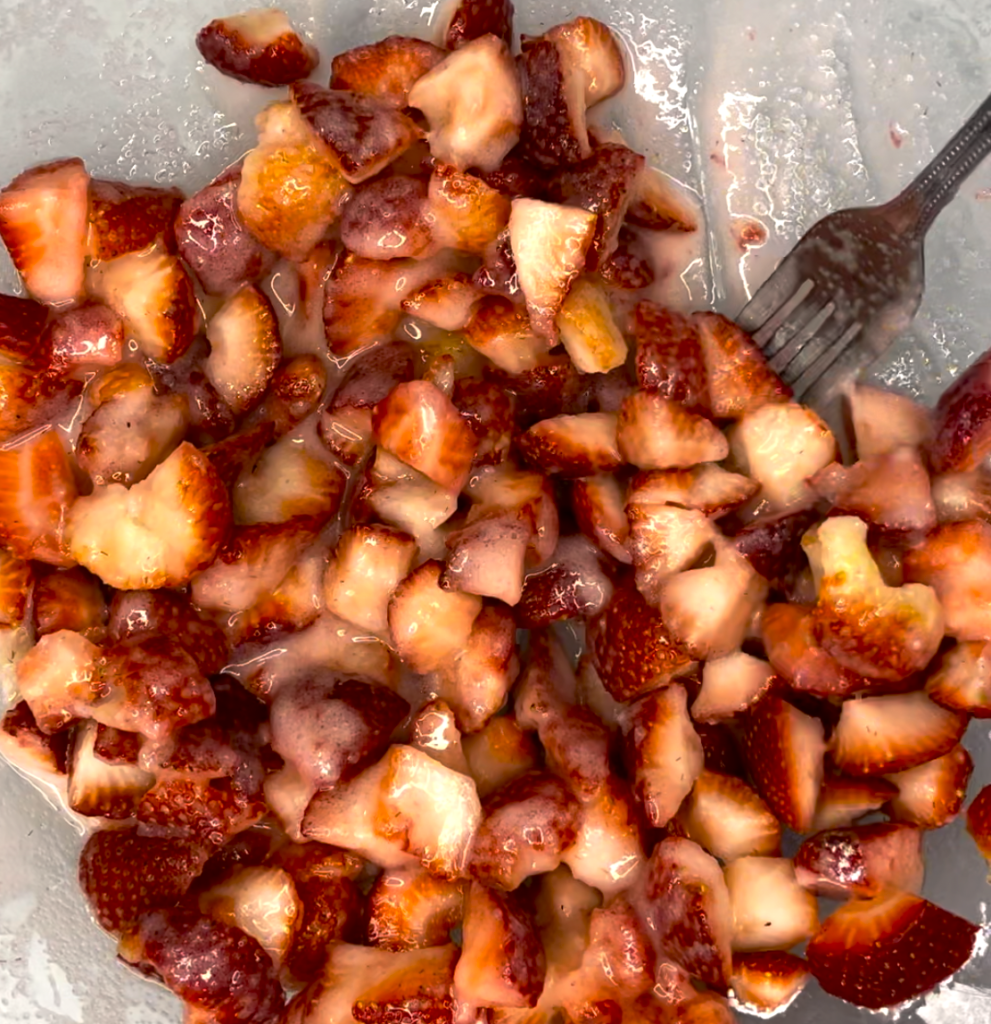 close up of the fresh strawberries in a glass bowl in the sugar mixture.