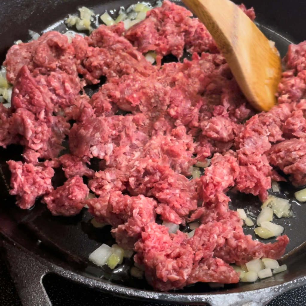 Adding hamburger to the cast iron pan with the garlic and onions