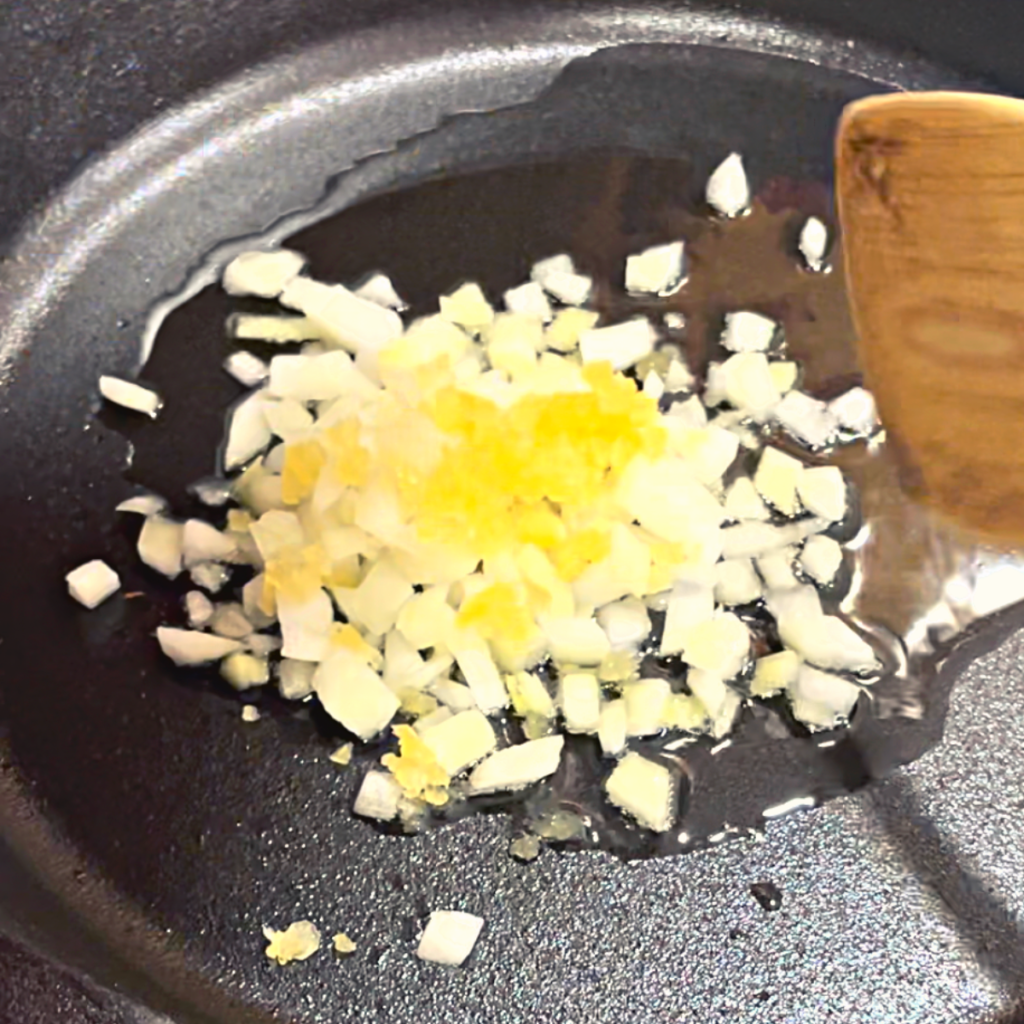 cast iron pan with onions and garlic being sauteed in oil.
