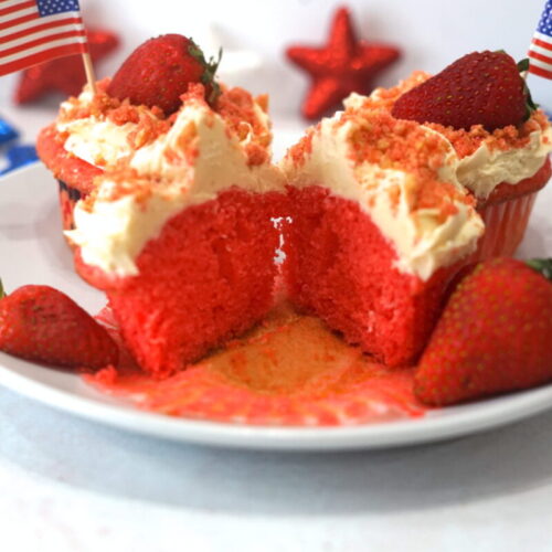 Strawberry crunch cupcake on a white plate cut in half with a strawberry on top and small usa flag stuck in the top.