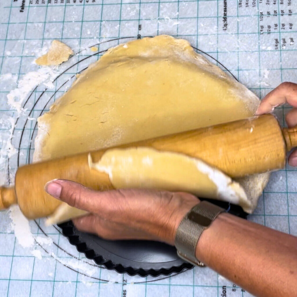Dough hung over the rolling pin laying it into the tart pan